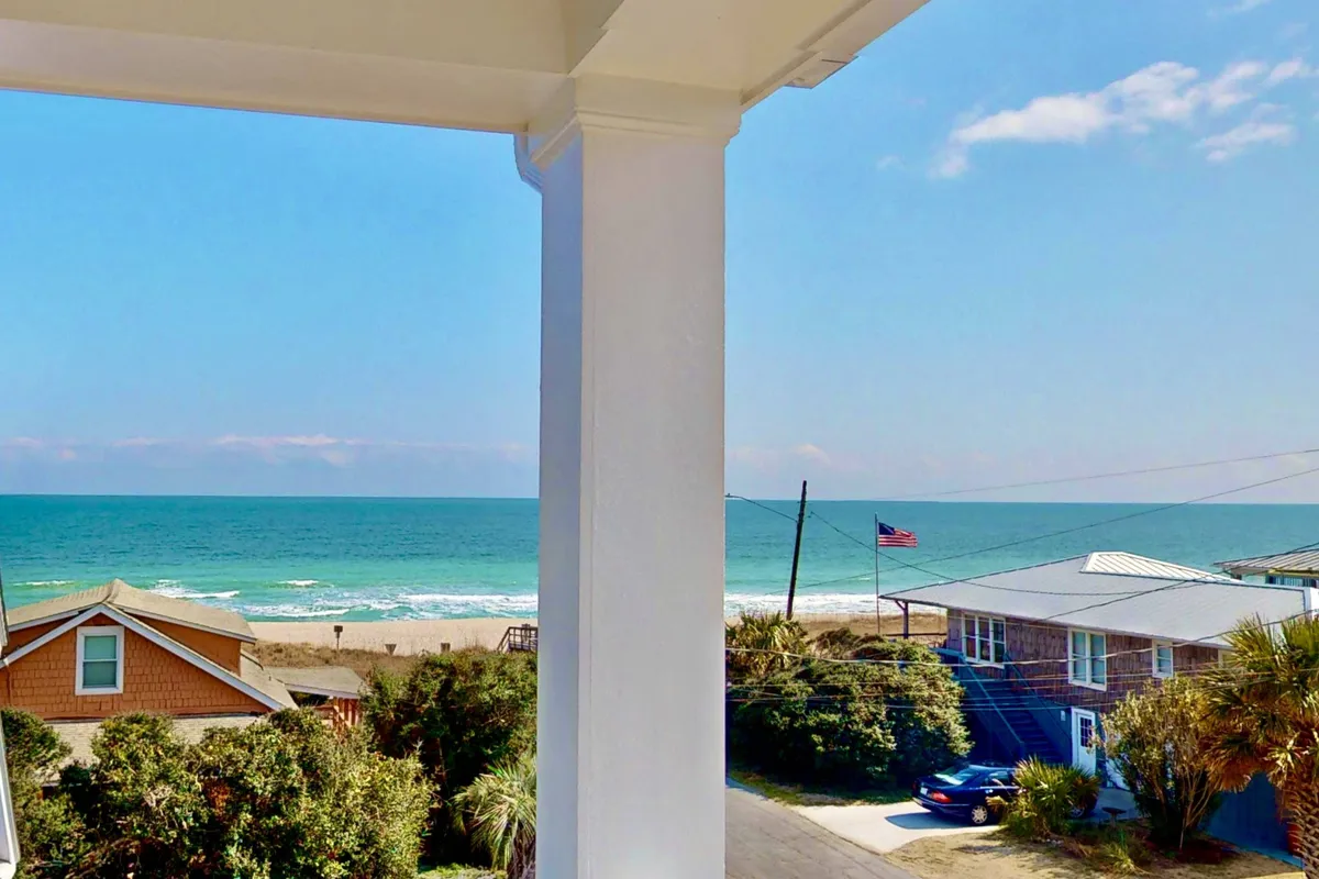 A sweeping view of the ocean and sandy beach, fringed by palm trees and nearby houses. The setting is lively yet relaxed, perfect for family gatherings and beach activities. The scene hints at families building sandcastles, swimming, and enjoying barbecues with a view of the water.