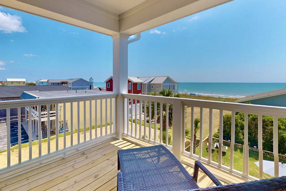 A serene ocean-facing balcony with comfortable outdoor furniture, a balcony railing, and sweeping beach views. The setup invites relaxation and social gatherings, and suggests proximity to the sand and water.
