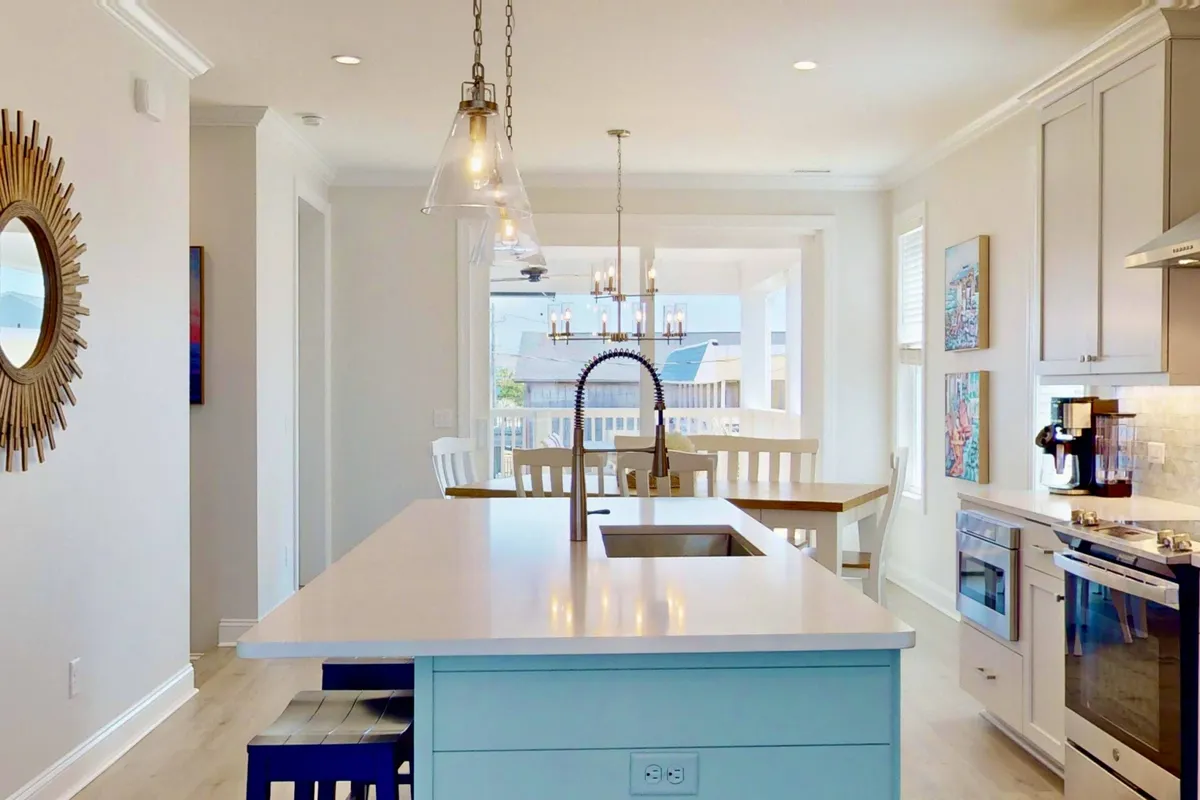 A bright, open-plan kitchen and dining area with an island countertop, modern fixtures, a spacious dining area, and artwork on the walls. The space is clearly designed for cooking, dining, and socializing, with ample room for larger groups to gather.