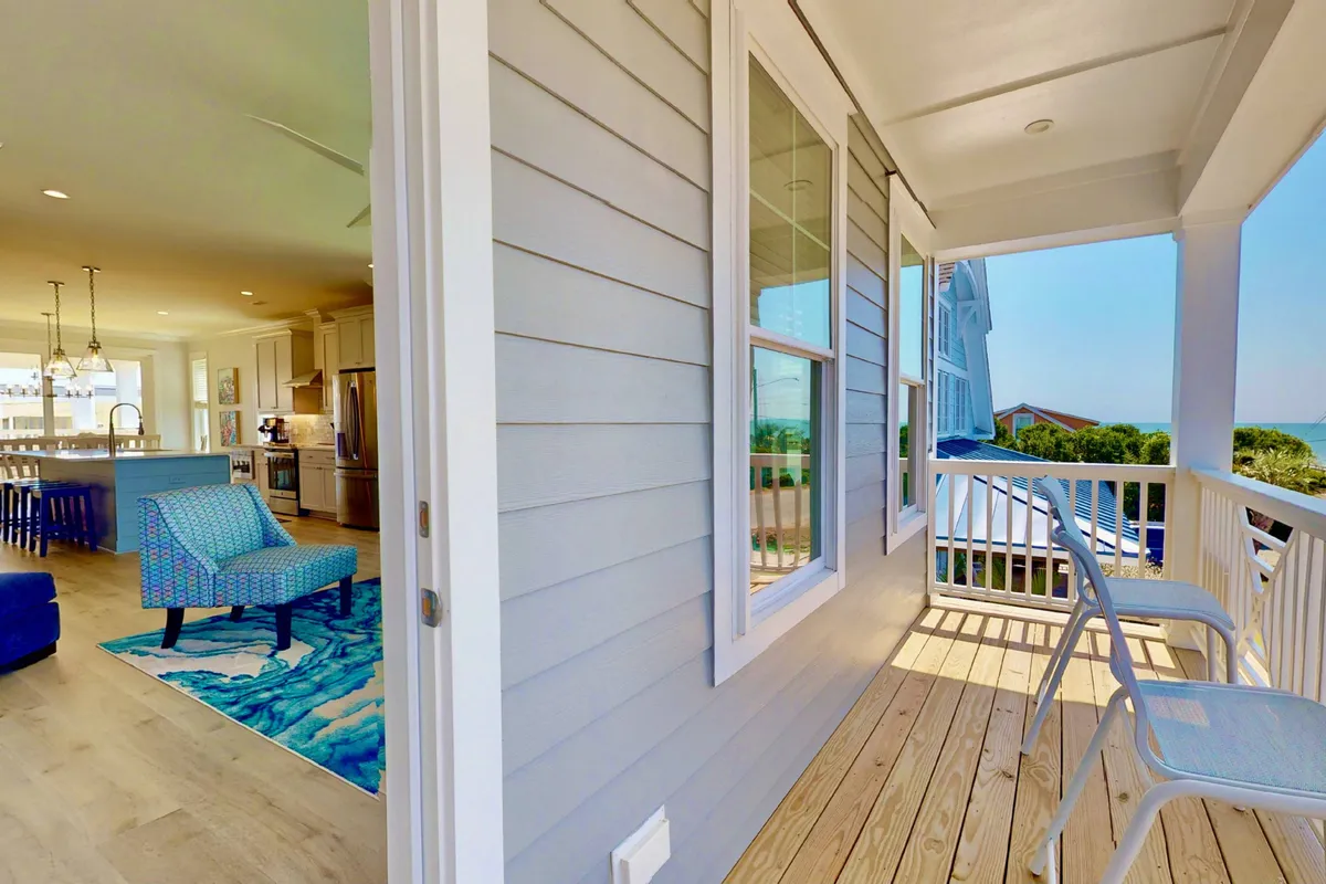 A welcoming exterior deck scene featuring a blue patterned chair, wooden railing, and an expansive view beyond the porch. The space is designed for relaxation—perfect for enjoying coffee at sunrise, reading, or gathering with friends for a barbecue.