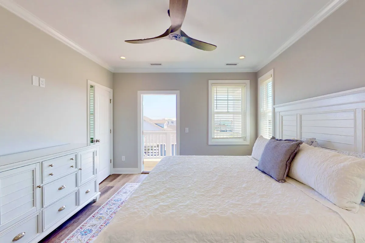 A tranquil bedroom scene with a bed adorned with decorative pillows, a window letting in morning light, and a ceiling fan for added comfort. The inviting setup suggests a restful space ideal for peaceful nights and rejuvenating mornings.