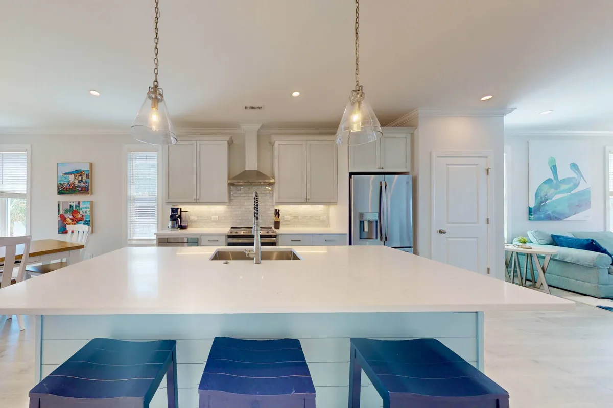 A stylish kitchen with a prominent island, blue bar stools, wall artwork, and gleaming stainless steel appliances. The space is open, airy, and designed for both cooking and socializing with family or friends.