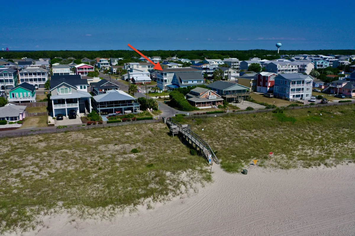 A relaxed beachfront property with a wooden boardwalk leading toward the water, surrounded by a residential area. The scene captures the property’s proximity to the beach and suggests ample space for family or group activities like beachcombing and evening gatherings.